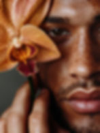 Close-up of a person's face with freckles, holding a vibrant orange orchid with red spots. The mood is serene and contemplative.